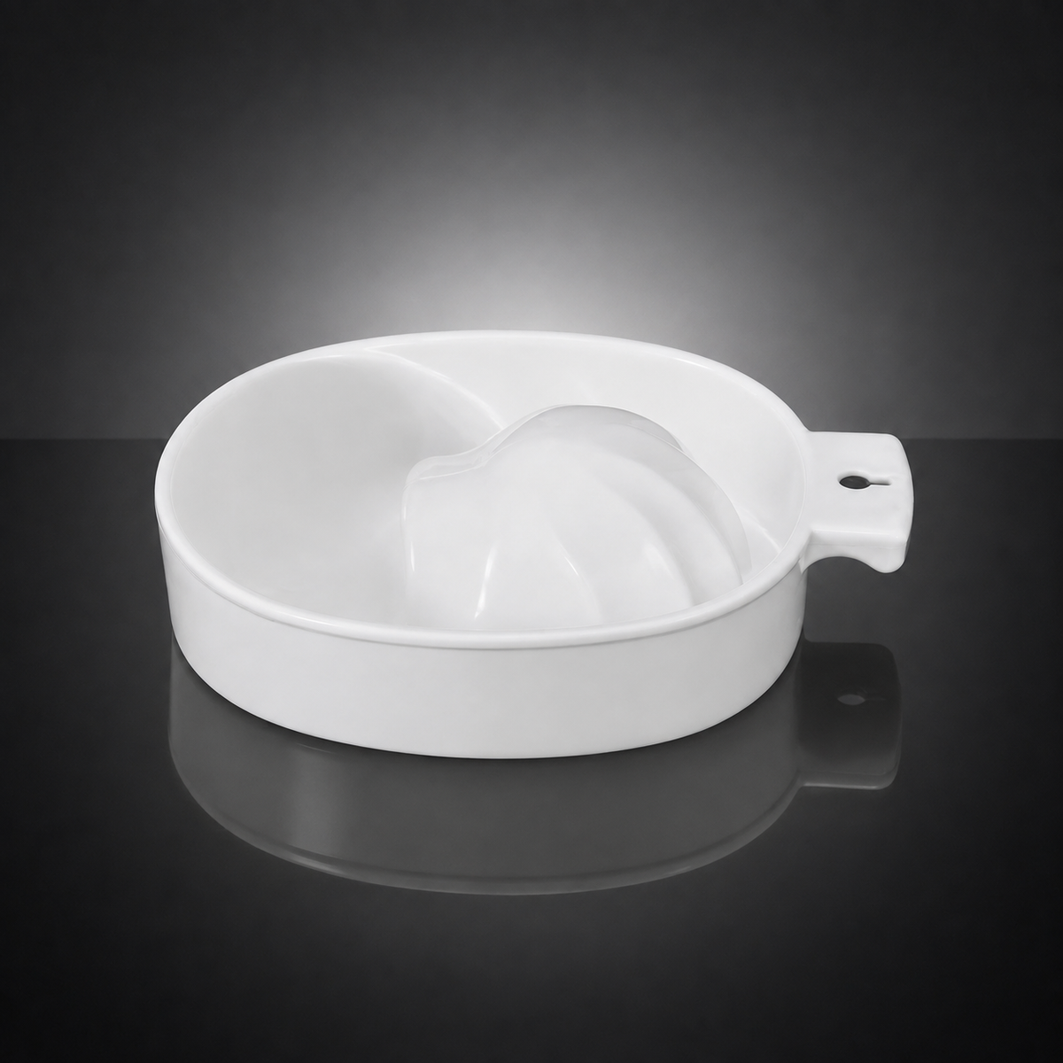 A white ceramic citrus juicer bowl with a handle, shown on a reflective dark gray surface against a black gradient background.