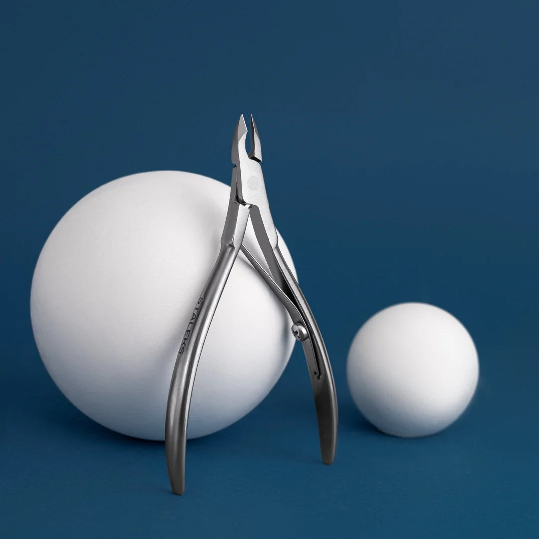 Full view of the Staleks Classic 12 cuticle nipper with 5mm half jaw against a dark blue studio background with white display spheres.