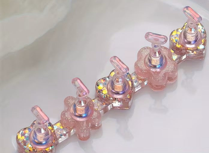 A pink glittery resin bracelet featuring five flower-shaped links with clear pump bottle details and iridescent holographic glitter accents, resting on a white surface.