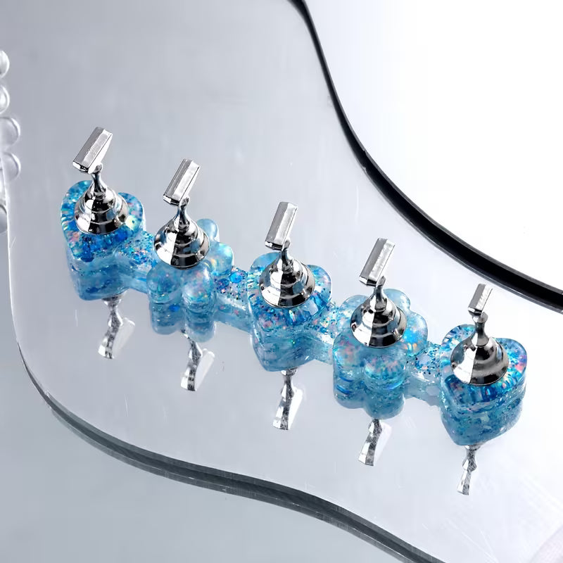 Five decorative faucet handles arranged in a row on a curved mirrored surface. The handles have blue and silver iridescent flower-shaped bases with metallic silver tops.