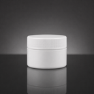 A plain white plastic cosmetic jar with a ribbed screw-on lid, centered on a dark gray reflective surface.