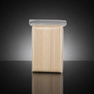 A clear plastic resealable bag containing a bundle of light beige wooden toothpick handles or toothpick-related sticks, photographed upright on a dark reflective surface against a black-to-gray gradient background.