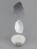 A white ceramic bowl with a small black logo, shown with its lid and a matching white scoop floating above it against a neutral gray background.