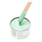 A metal tin of Satin Smooth hair wax in a mint green color, with a wooden spatula coated in the wax resting inside the tin on a white background.