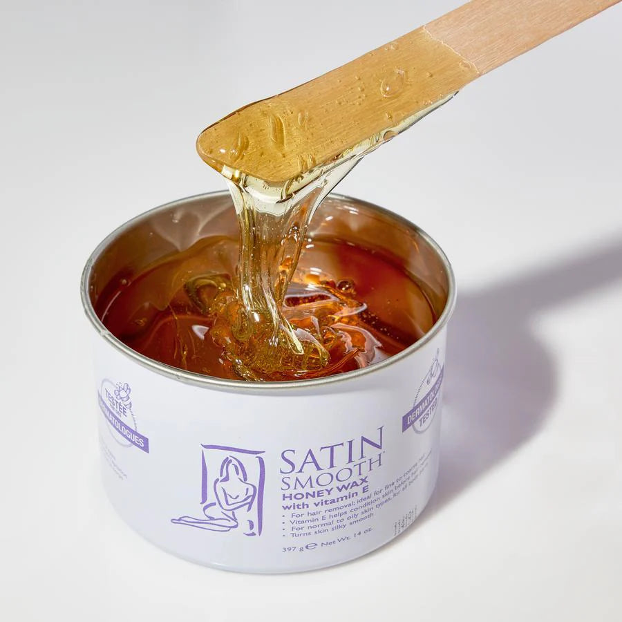 Can of Satin Smooth Honey Wax with a wooden applicator dripping wax onto a white background