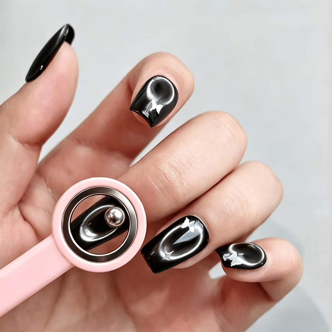 Hand with black nail polish holding a pink and silver object against a gray background