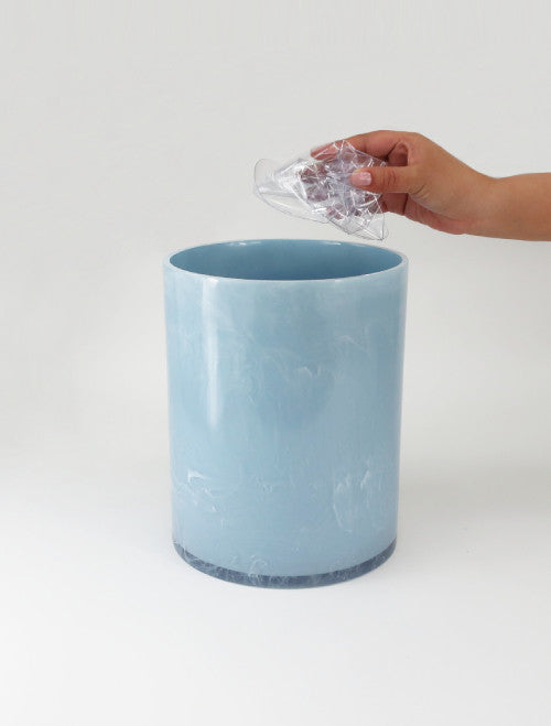 Blue trash can with a hand disposing of plastic waste on a white background